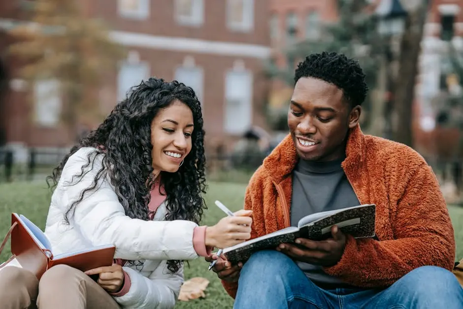 Happy college students studying together on a campus lawn, sharing ideas and writing notes.