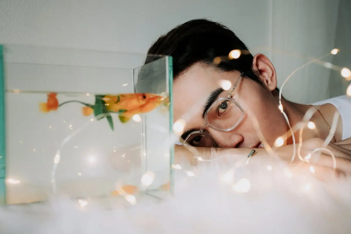 Man Leaning on Table Near Aquarium and Fairy Lights