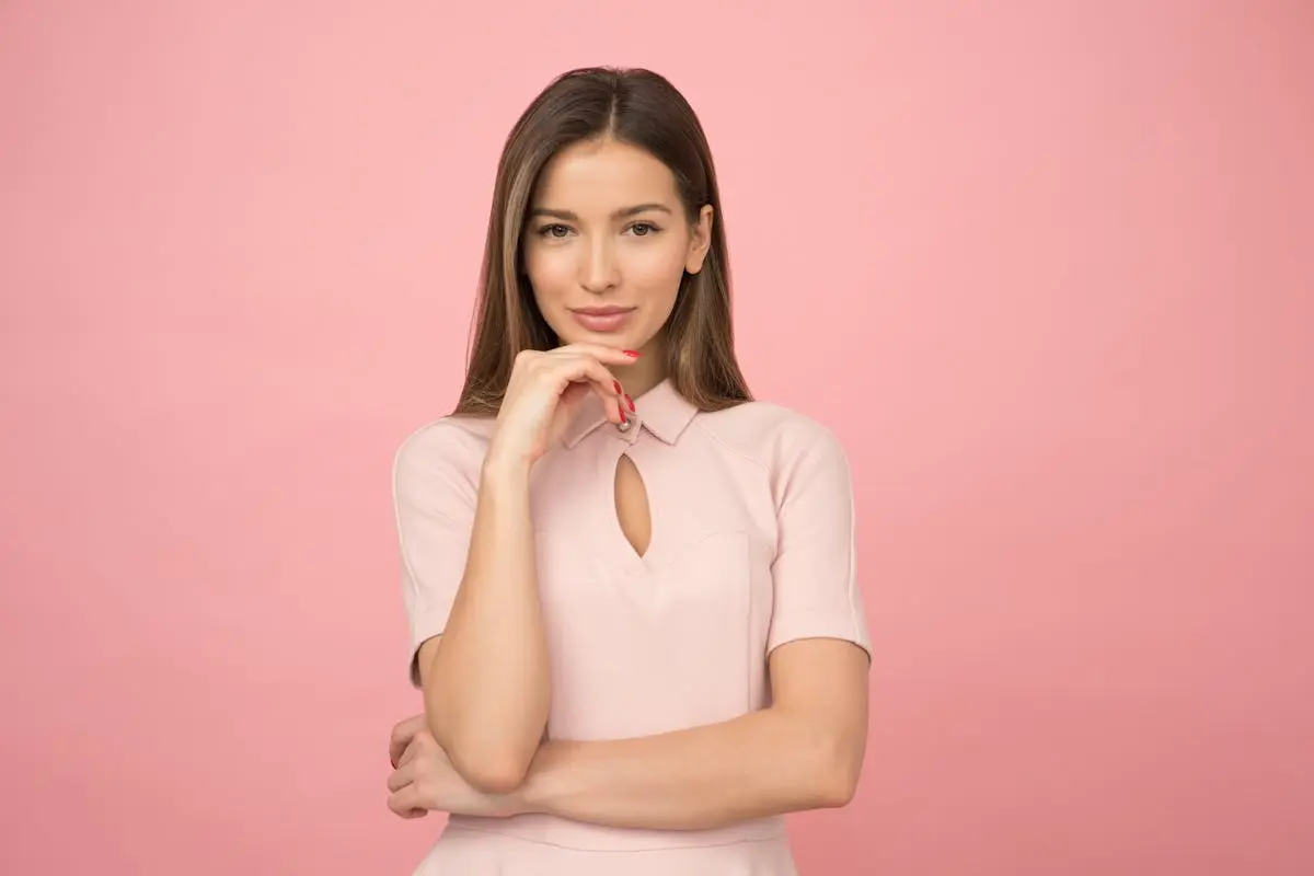 Portrait of a young woman posing elegantly in a studio with a pink background.