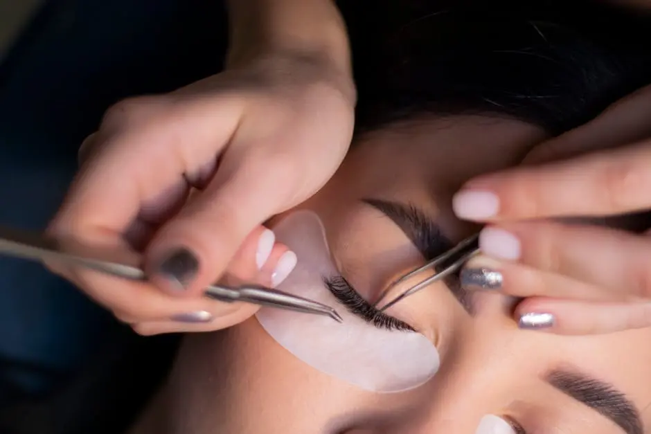 Detailed view of a beautician applying eyelash extensions to a woman’s eyes.