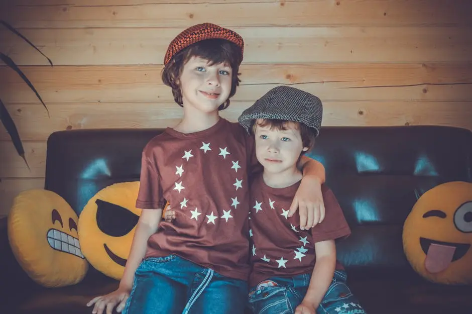 Two boys sitting on a sofa, smiling in matching star shirts and hats, surrounded by emoji pillows.