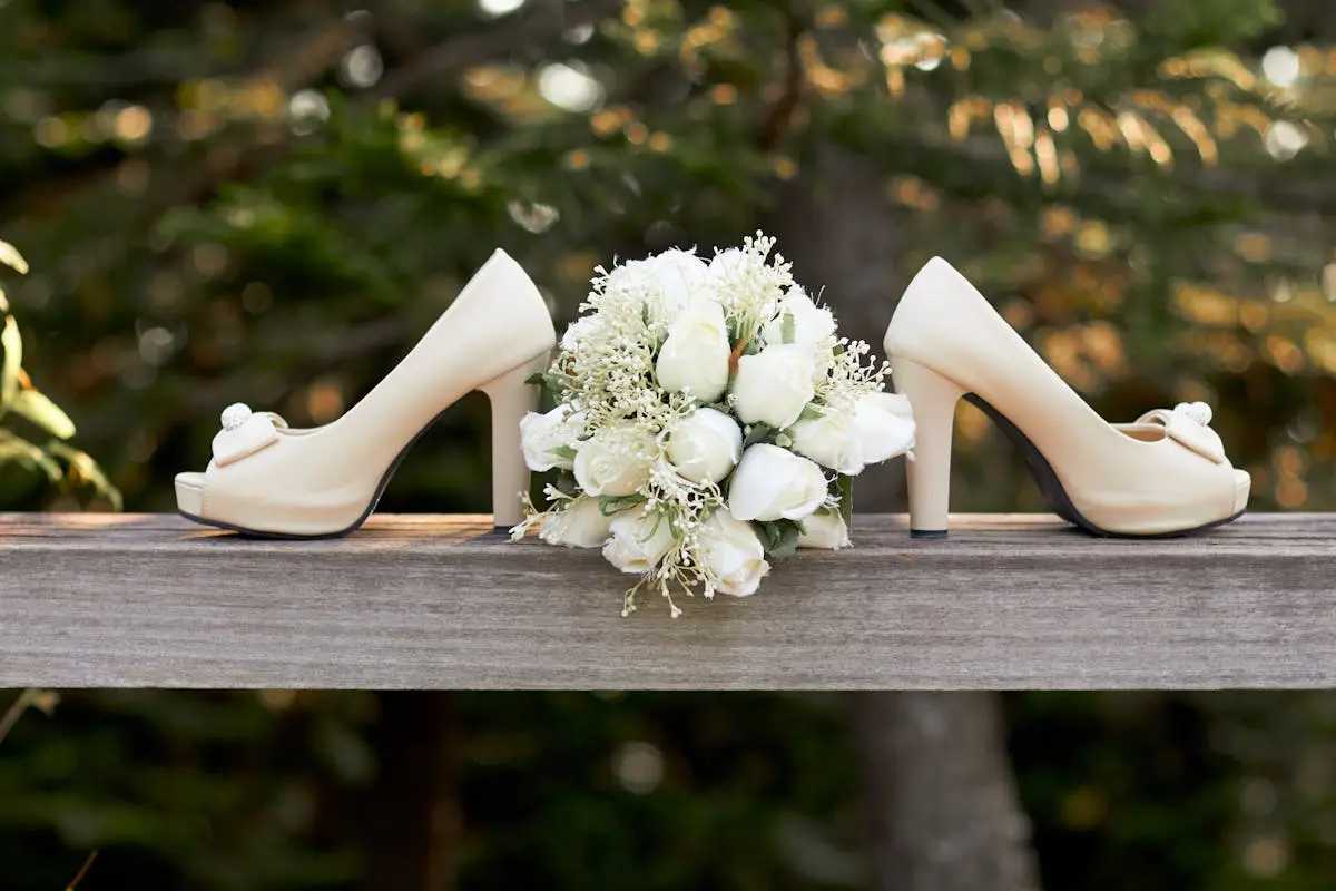 Selective Focus Photography of Pair of White Open-toe Chunky Heeled Shoes and Bouquet Flowers