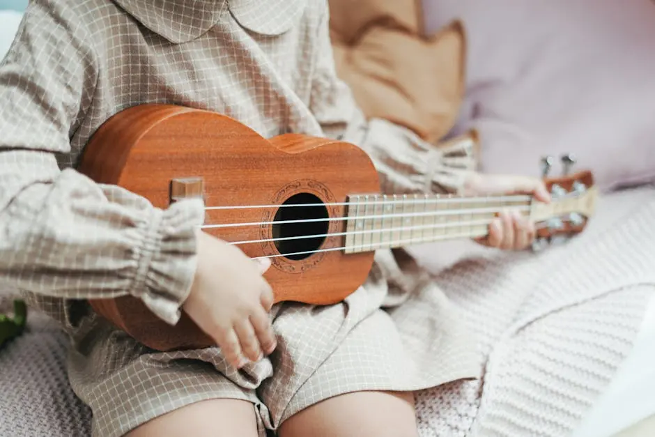 A child strums a wooden ukulele indoors, capturing a serene musical moment.