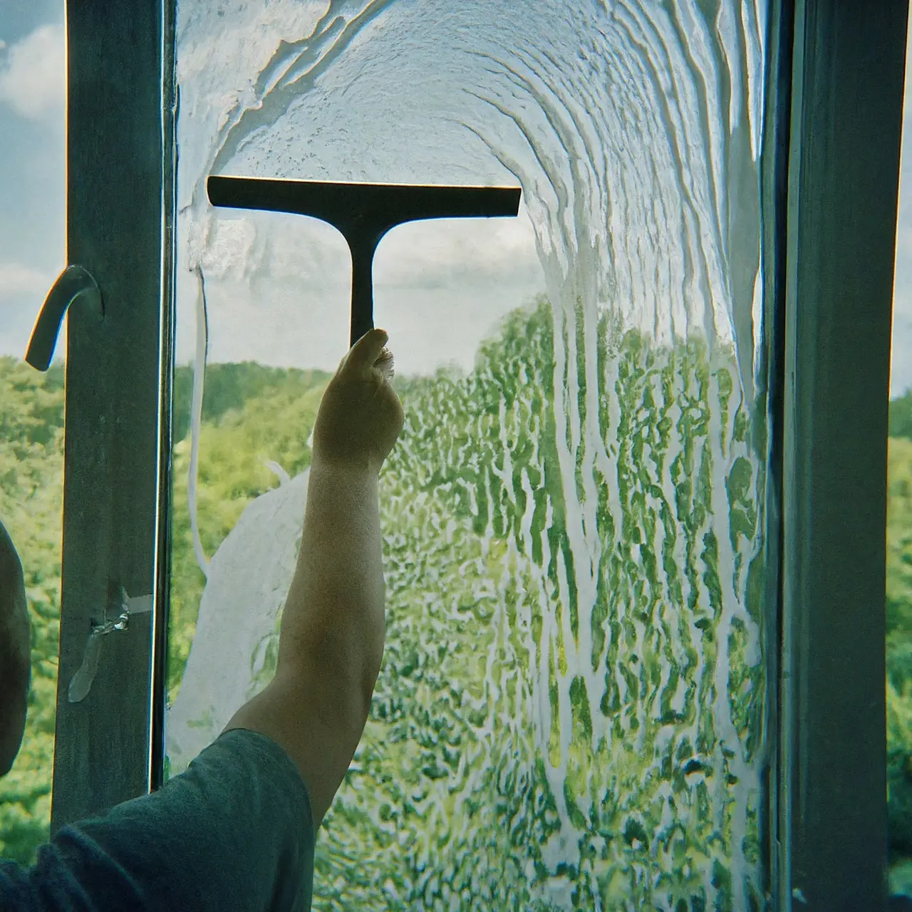 A person cleaning a high window with a squeegee. 35mm stock photo