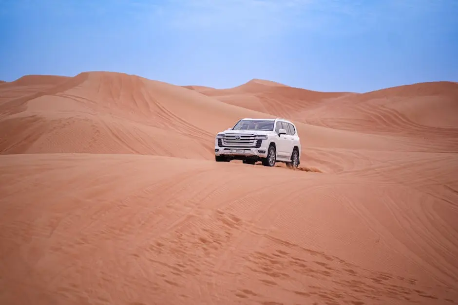 A white SUV traverses the expansive and serene desert dunes under a clear blue sky.