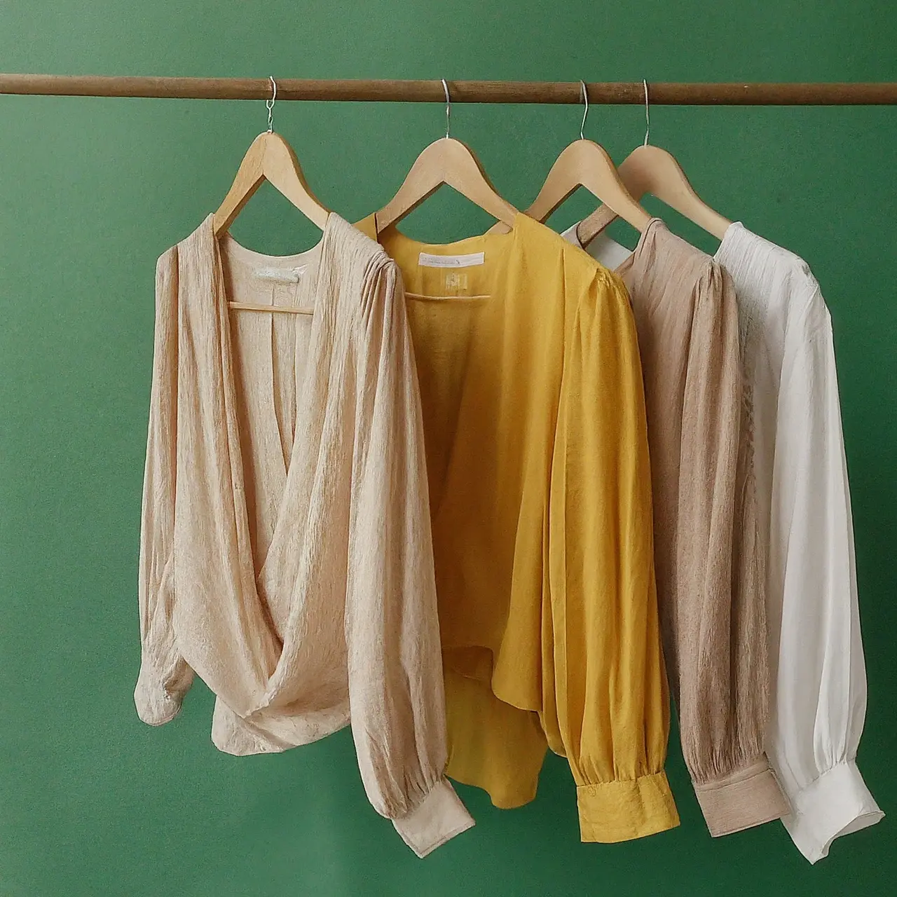 Elegant blouses hanging on wooden hangers against a green backdrop. 35mm stock photo