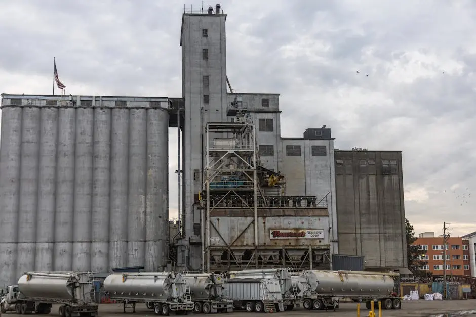 An industrial facility with large storage silos and parked tanker trucks under a cloudy sky.