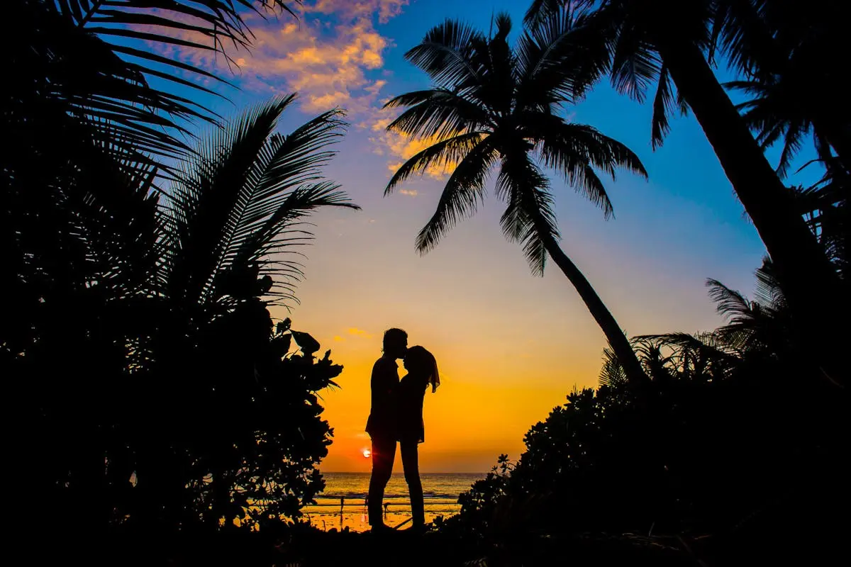 Silhouette of a couple sharing a romantic moment on a tropical beach at sunset with palm trees.