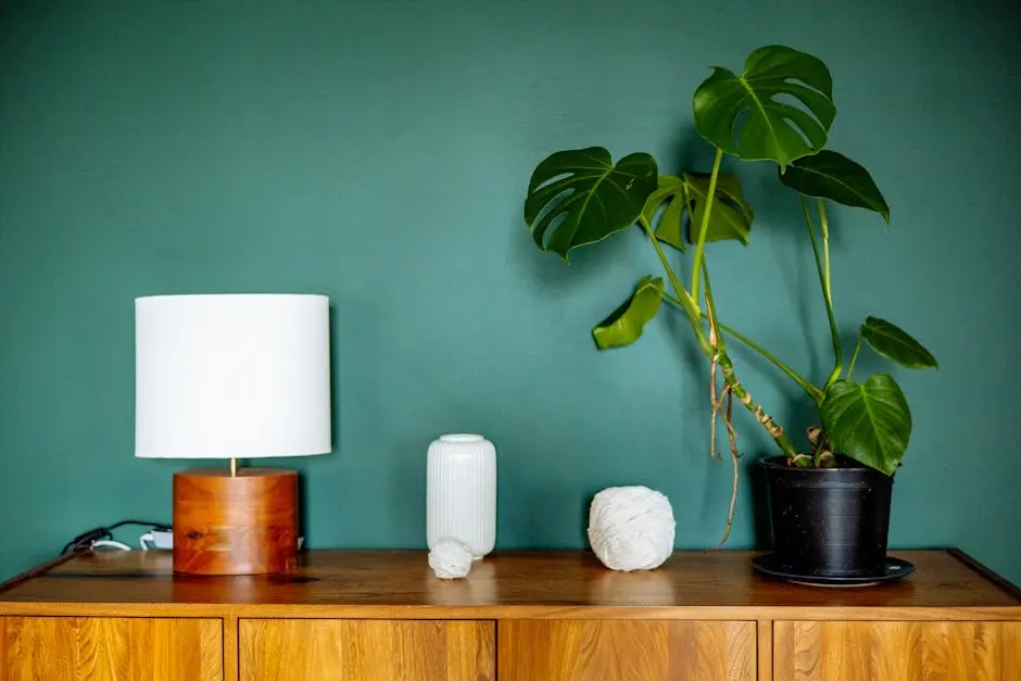 A stylish wooden dresser with a monstera plant, lamp, and decor against a green wall.