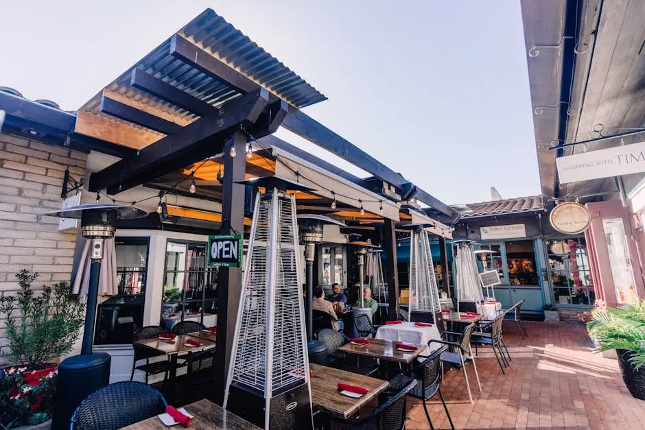 Sunny outdoor restaurant setting with tables, chairs, and heaters under a modern pergola.