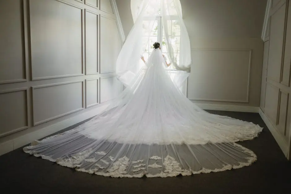 A bride in a wedding dress stands in front of a window