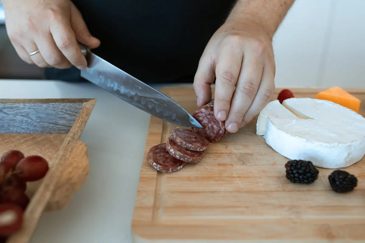 A Person Slicing Salami on a Wooden Chopping Board