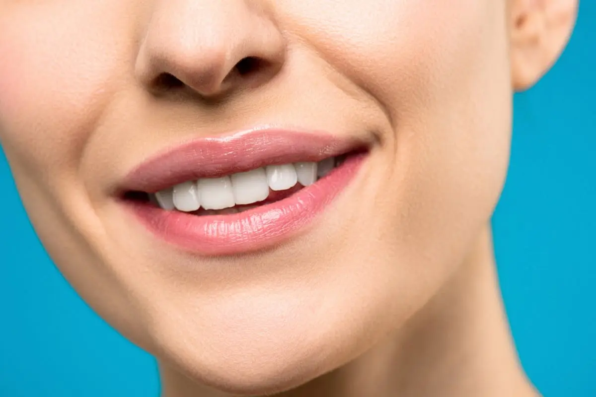 A close-up image of a woman’s smile with pink lipstick and white teeth against a blue background.