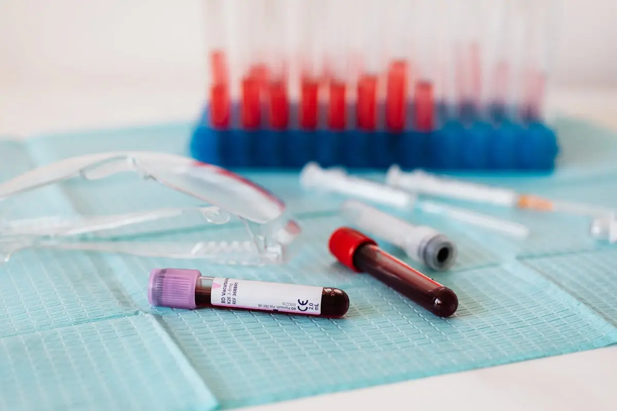 Closeup of full vials of blood placed on medical diaper near plastic eyeglasses and syringes and test tubes in container