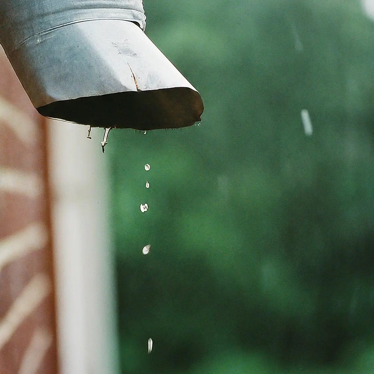 A close-up of a damaged house downspout during rain. 35mm stock photo