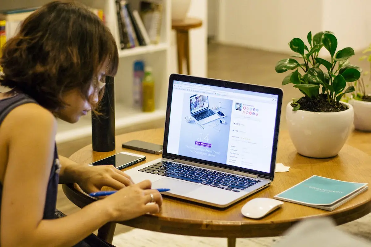 Woman in Black Tank Shirt Facing a Black Laptop Computer on Brown Wooden Round Table in an Ideal Student Lounge