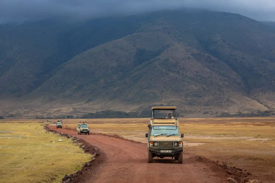 Safari jeeps drive on a red dirt road through the Ngorongoro Crater with mountainous backdrop.