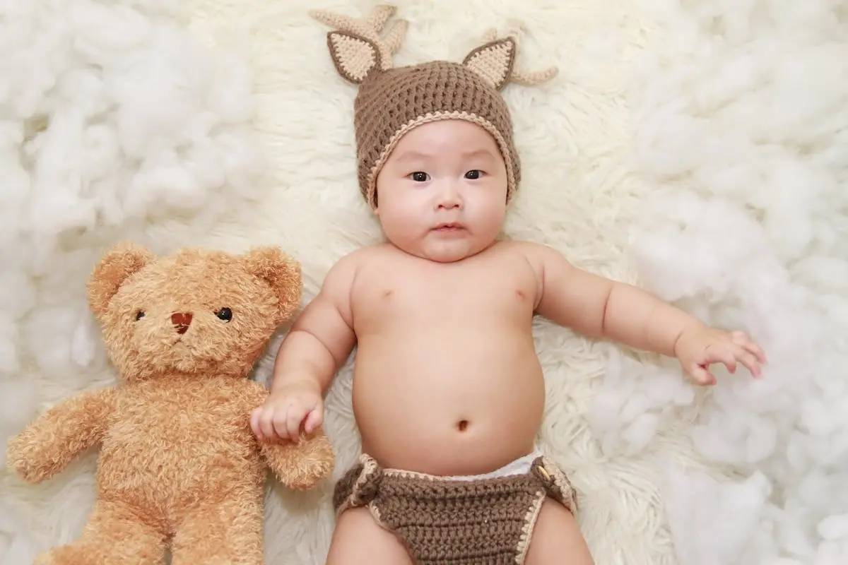 Baby Lying on White Cushion Beside Brown Bear Soft Stuffed Animal