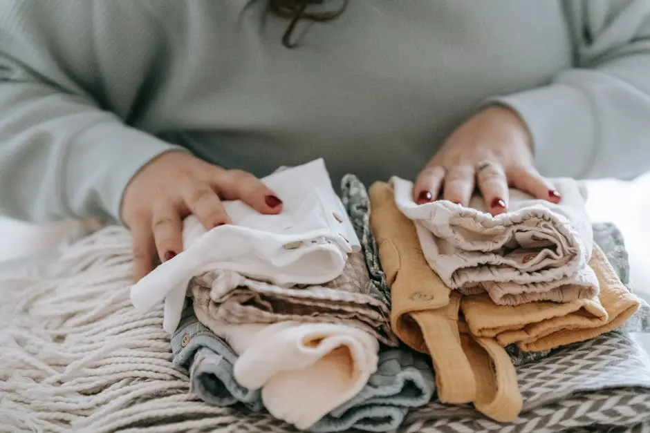 Crop faceless female with manicure arranging baby clothes on warm scarf while sitting at table in light room at home