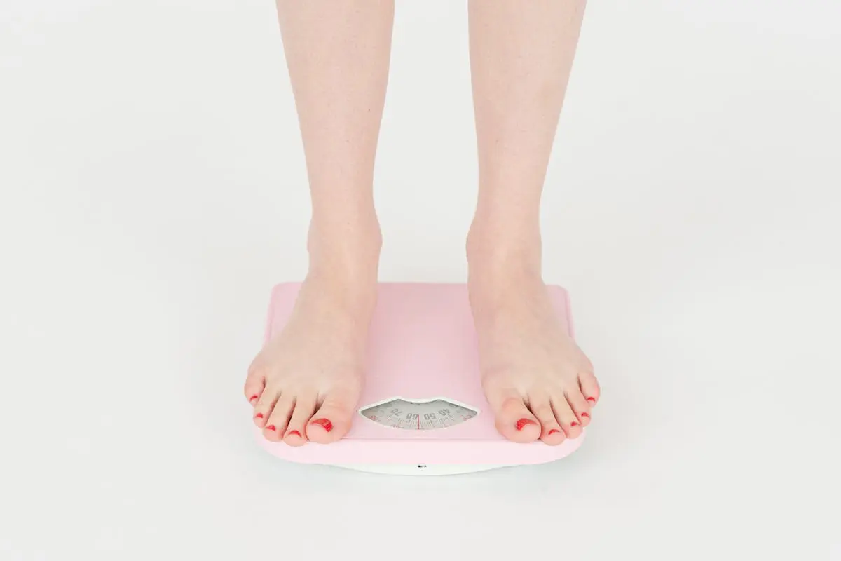 High angle of crop anonymous female measuring weight for control body against white background in studio