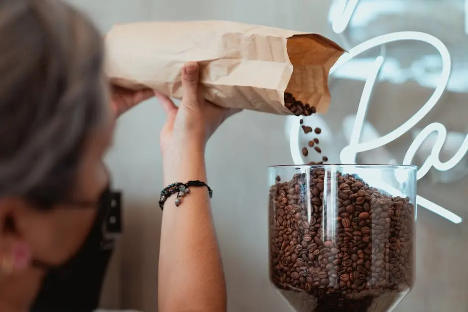 Close-up of a barista pouring fresh coffee beans into a grinder with a paper bag.