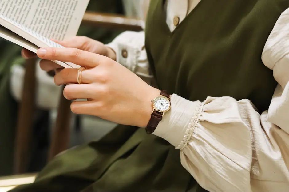 Close-up of a woman in an olive dress reading a book with a classic watch and ring.