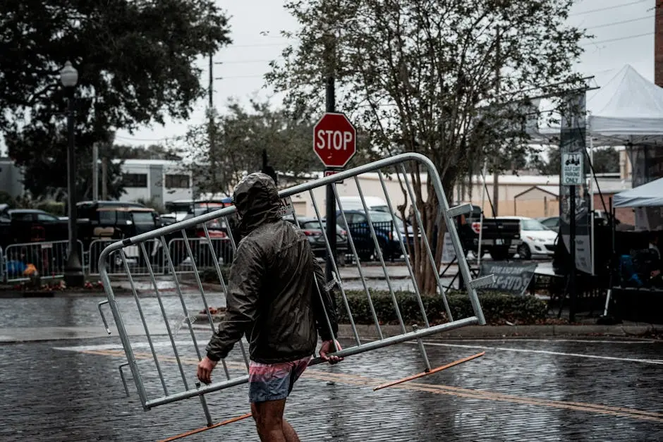 A person in a raincoat carrying a barrier on a wet city street on a rainy day.