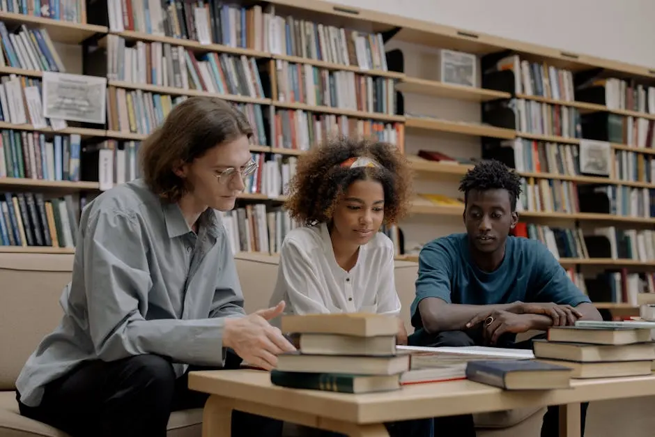 Three students studying together in a library, surrounded by books and learning materials.