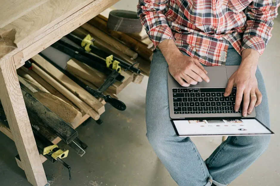 A craftsman using a laptop in a woodworking workshop, focusing on online research or design.