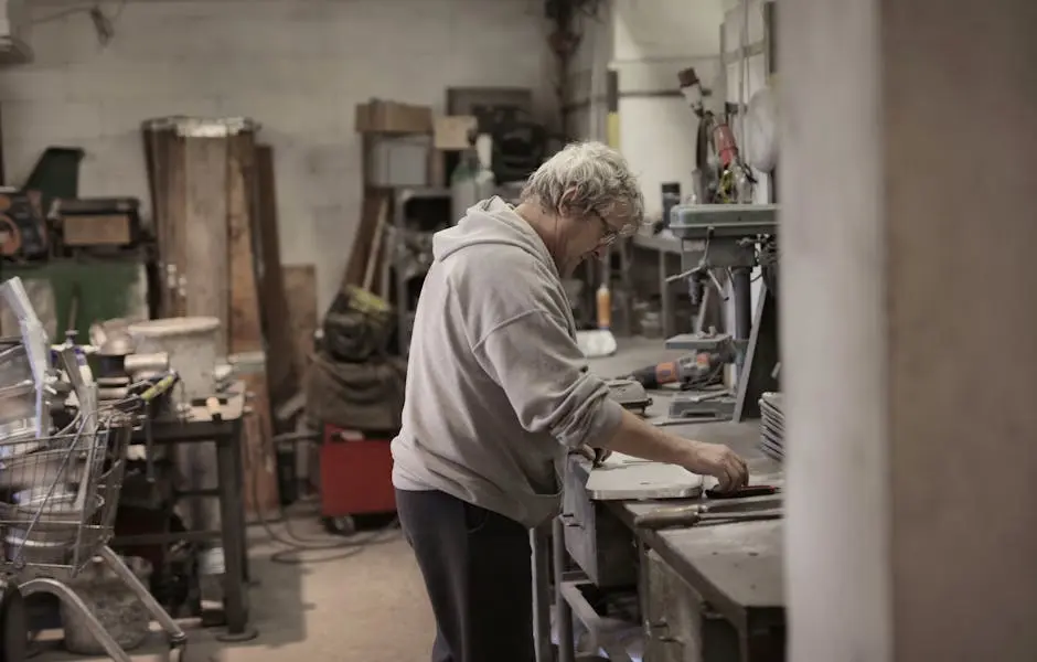 Side view of aged white hair craftsman in eyeglasses using workbench for detail handling in workshop