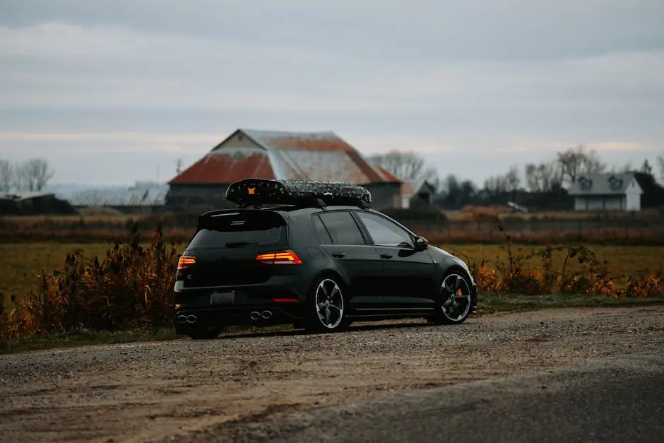 A stylish black hatchback with roof rack parked on a dirt road in a rural setting during autumn.