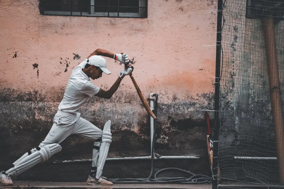 Cricket player in sportswear practicing with bat, wearing full gear against an urban backdrop.