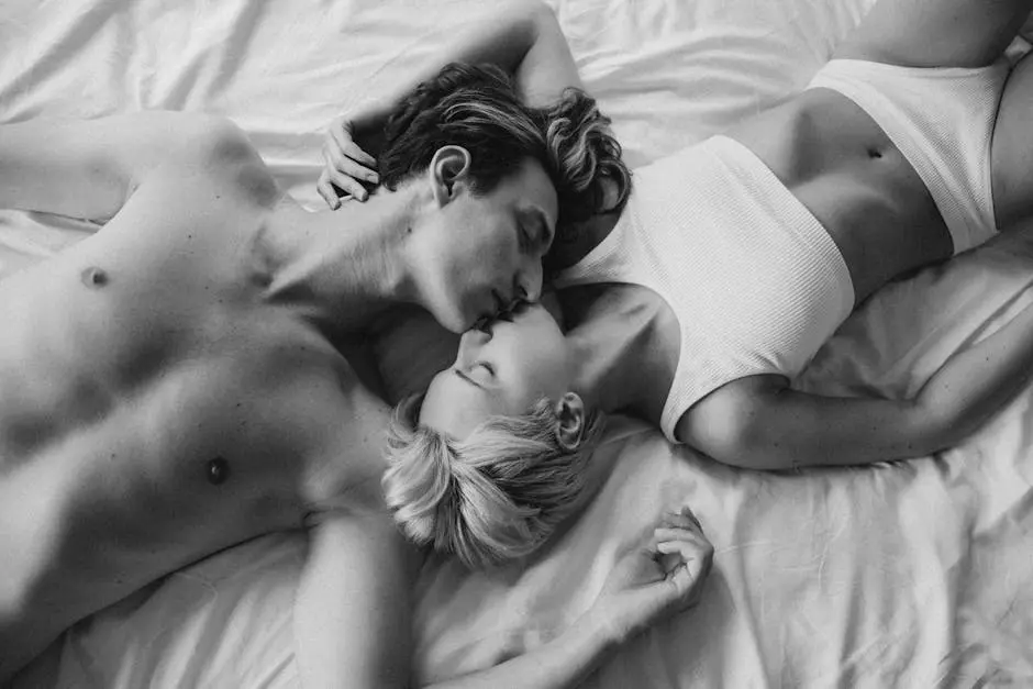 Black and white photo of a couple kissing and embracing on a bed, showcasing intimacy.