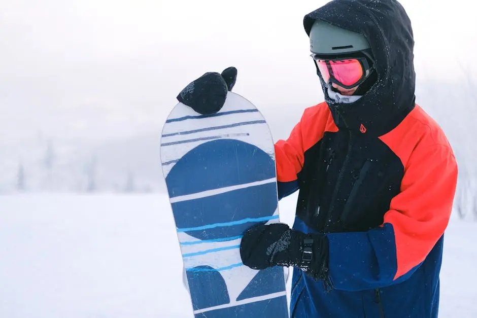 A snowboarder with reflective goggles holding a snowboard in the snowy outdoors.