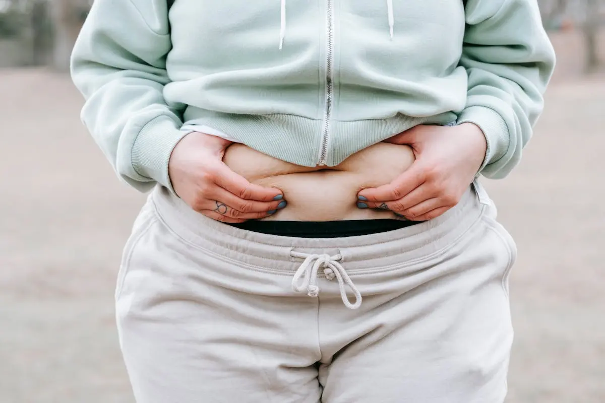 Close-up of a person in casual clothing holding their stomach to illustrate body contouring. The image highlights body contours and sculpting, emphasizing the natural shape and form. Perfect for discussions about body contouring, body sculpting, and the benefits of contouring techniques