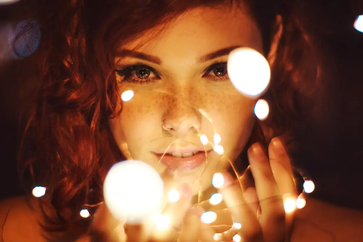 Enchanting close-up of a woman with red hair and freckles surrounded by glowing fairy lights.