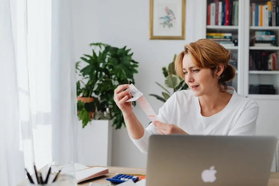 Woman Sitting Behind a Desk Using Laptop and Looking at Items on a Receipt