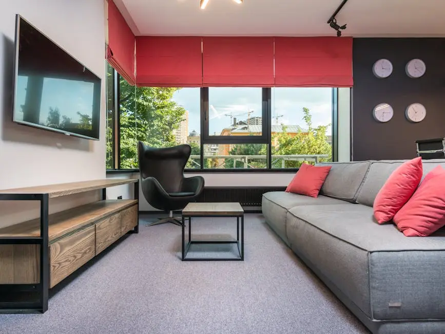 Contemporary lounge interior with couch and leather armchair against window and wall with clocks in workspace