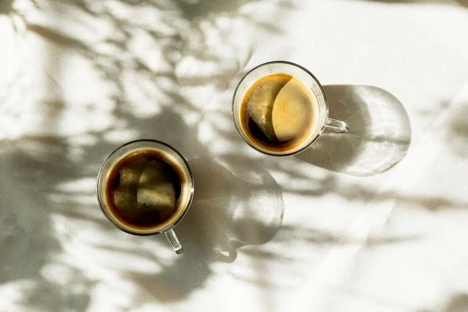 Two glass cups of espresso casting artistic shadows on a sunny table.