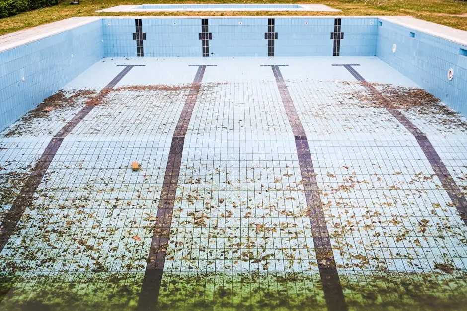 High angle view of an empty, abandoned swimming pool with leaves scattered on the tiled surface.