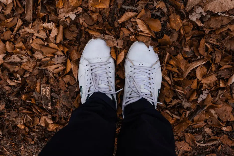 White sneakers standing on a bed of fallen autumn leaves from an overhead perspective.