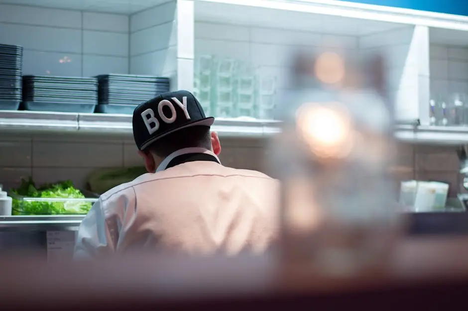 A chef wearing a BOY cap is seen working in a modern kitchen, focusing on food preparation.