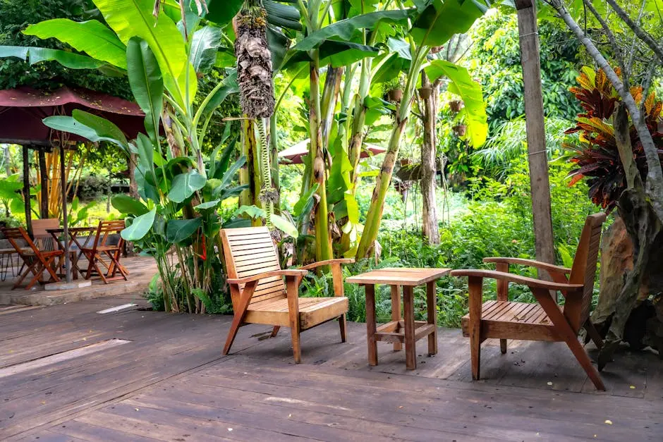 Two wooden chairs sitting on a wooden deck in the middle of a tropical garden