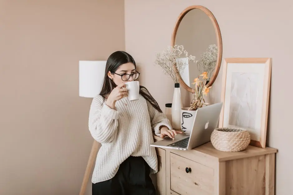 Une jeune femme savoure un café tout en travaillant sur son ordinateur portable dans un environnement domestique confortable.