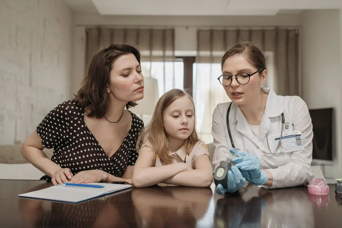 A healthcare professional demonstrates blood sugar monitoring to a mother and daughter at home.