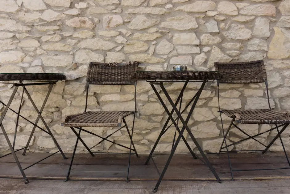 Three wicker chairs and a table against a stone wall