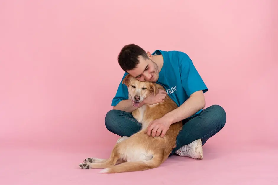 Smiling man in blue shirt hugging a happy dog on pink studio floor, enjoying companionship.