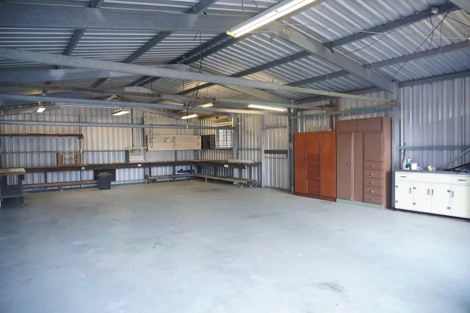 Empty industrial garage with steel walls and ceiling, featuring storage cabinets and workbenches.