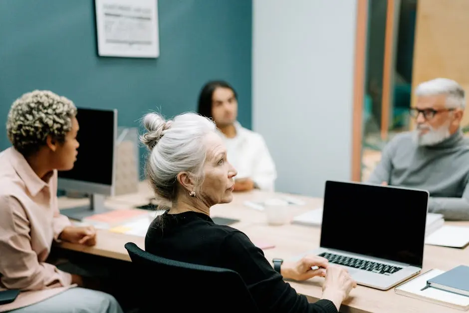 A multicultural team engaged in a meeting around a conference table with laptops.