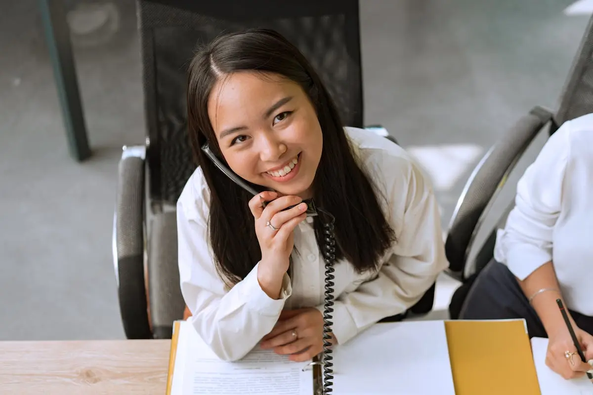 Asian woman smiling while talking on a phone in a modern office setting.